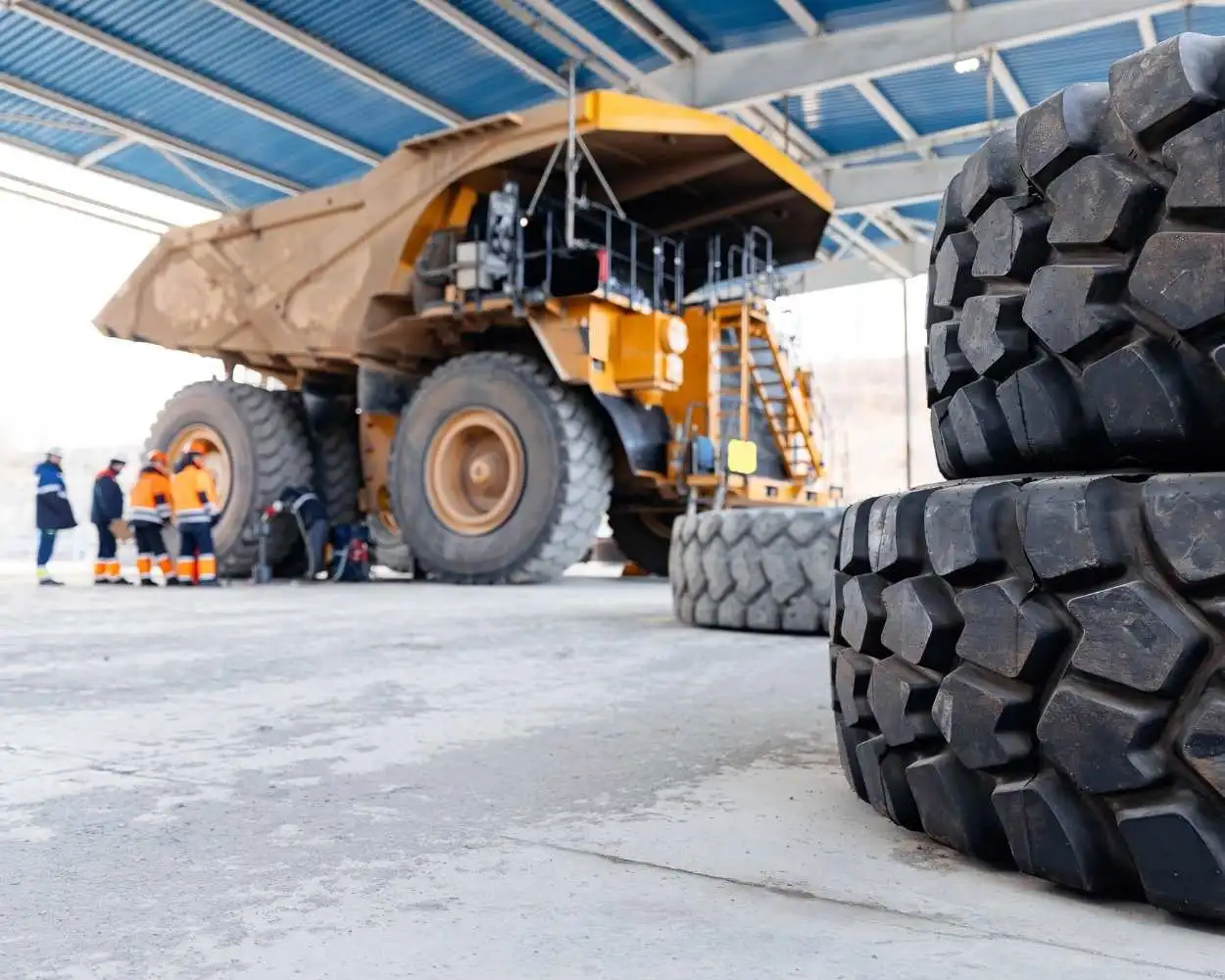 Technicians working in a garage with tires and a large industrial mining truck, providing specialized services for heavy-duty equipment