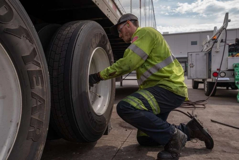 Technician changing heavy duty tractor trailer's tire in a maintenance yard.