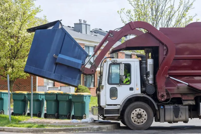 Front loader garbage truck lifts dumpster to empty into truck's waste compactor.